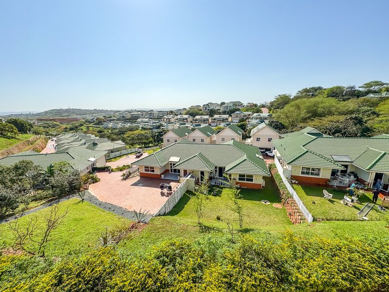 An elevated aerial view of a residential estate featuring multiple houses with green tiled roofs, paved driveways, and well-maintained garden spaces.