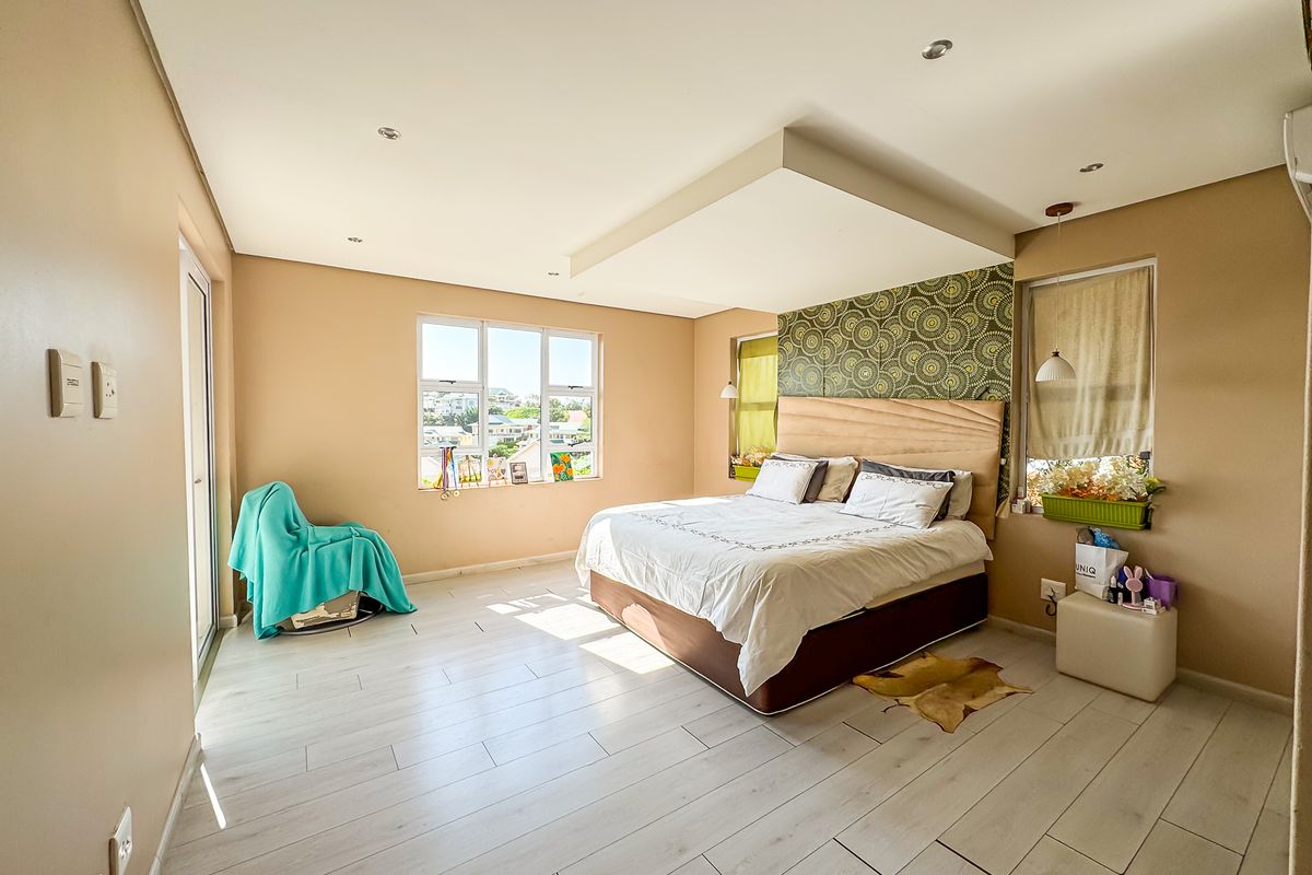 Spacious bedroom featuring light-toned laminate flooring, a recessed ceiling detail, and large windows providing natural light and exterior views.