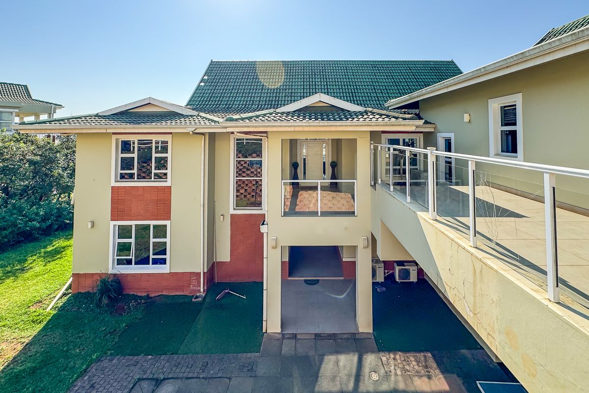 Rear view of a multi-level house featuring a tiled roof, a raised balcony with glass balustrades, and a paved patio area.
