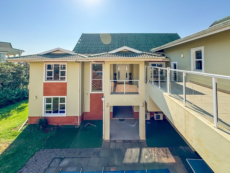 Rear view of a multi-level house featuring a tiled roof, a raised balcony with glass balustrades, and a paved patio area.