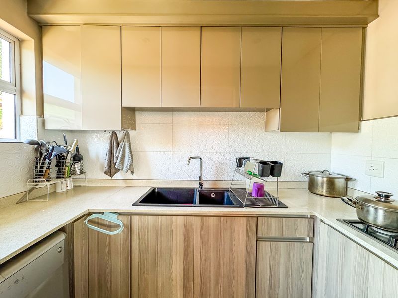 A functional kitchen featuring modern wood-grain lower cabinetry, sleek beige upper cabinets, a double basin sink, and a textured tile backsplash.