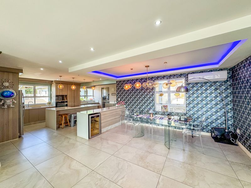 Spacious open-plan living and dining area featuring a modern kitchen with island, built-in appliances, tiled floors, and decorative feature wall with ambient lighting.