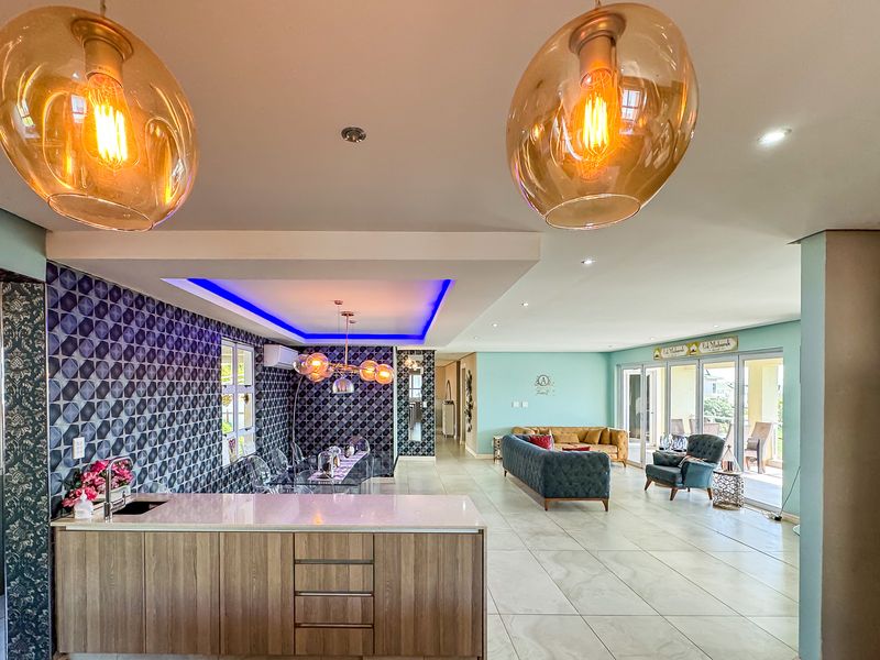 Spacious open-plan living area featuring a modern kitchen island, stylish tiled feature wall, recessed lighting, and large sliding doors leading to the outdoor space.