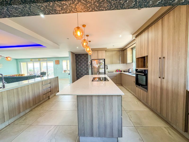 Modern open-plan kitchen featuring a large island with stone countertops, integrated cabinetry, built-in oven, and stylish pendant lighting, seamlessly flowing into the living area.