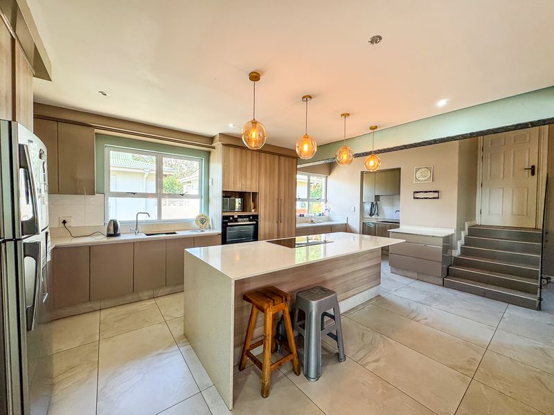Modern open-plan kitchen featuring a central island with quartz countertops, built-in oven, induction hob, and ample cabinetry, seamlessly connected to the living area.
