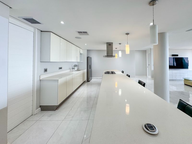 Modern open-plan kitchen featuring sleek white gloss cabinetry, stone countertops, integrated gas hob, and polished marble-look flooring in a bright, contemporary living space.