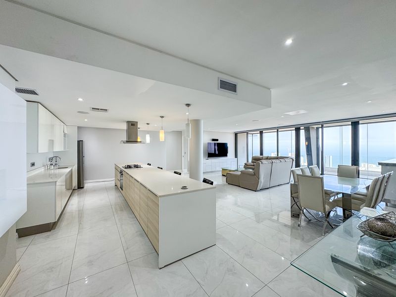 Spacious open-plan living area featuring a modern kitchen with a large island, sleek cabinetry, and floor-to-ceiling windows offering expansive views.