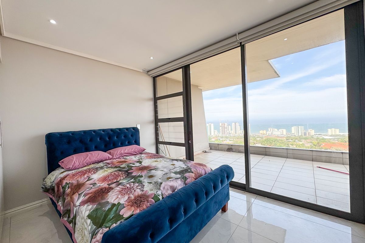 Spacious bedroom featuring large sliding glass doors that open onto a private balcony with expansive coastal and city views.