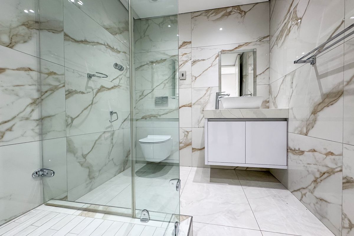 Modern bathroom featuring a glass-enclosed shower, wall-mounted toilet, and a floating vanity with a vessel sink, finished with elegant marble-look wall tiles.