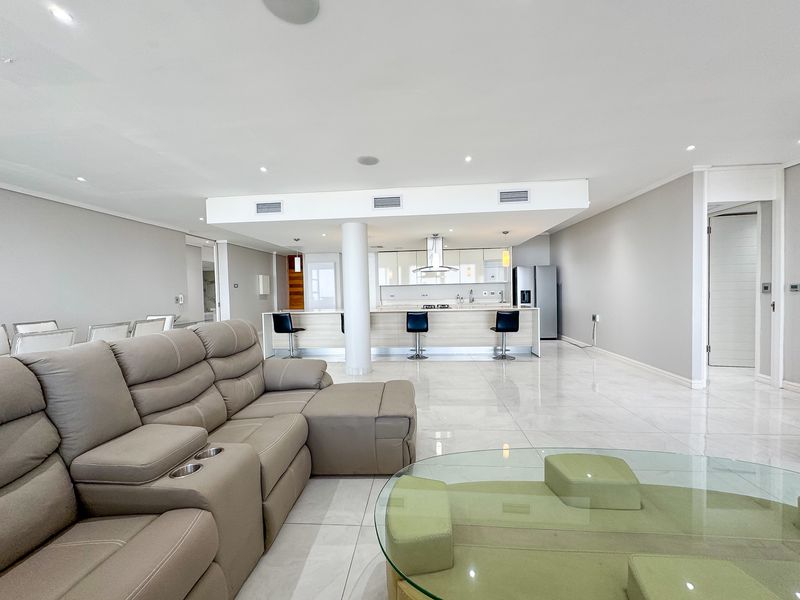 Spacious open-plan living and kitchen area featuring a large central island, modern cabinetry, recessed lighting, and polished tiled flooring throughout.