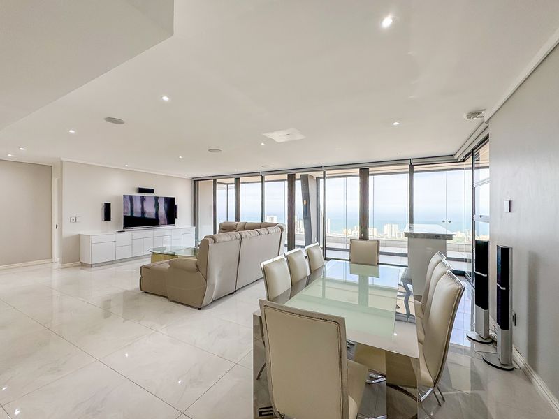 Spacious open-plan living and dining area featuring high-end marble-look flooring, recessed lighting, and expansive floor-to-ceiling glass doors offering panoramic ocean views.
