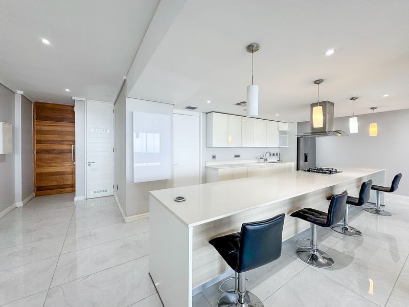 Modern open-plan kitchen featuring a large island with quartz countertops, gas hob, sleek cabinetry, and high-quality tiled flooring throughout the living space.