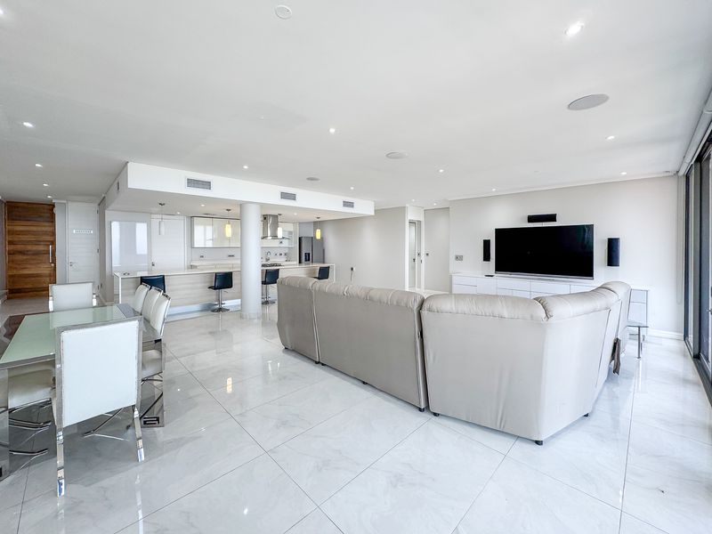 Spacious open-plan living, dining, and kitchen area featuring modern marble-look flooring, recessed lighting, and a sleek kitchen island with integrated appliances.