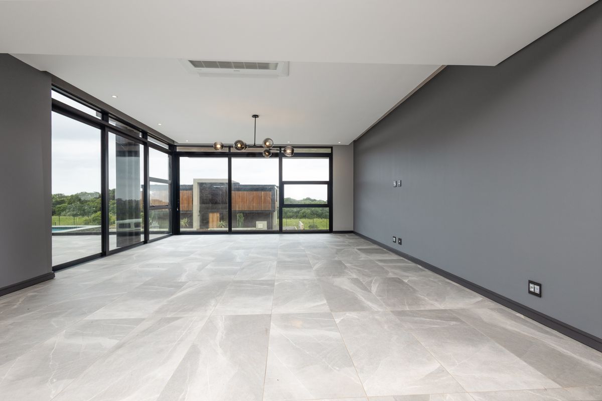 Spacious, modern living area featuring large format floor tiles, sleek grey walls, and expansive black-framed sliding doors offering abundant natural light and outdoor views.