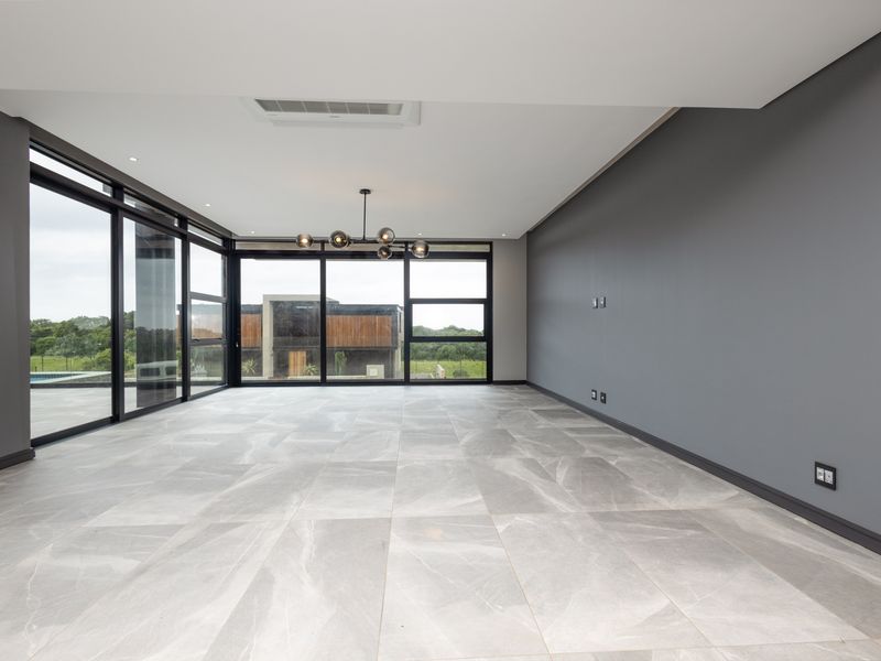 Spacious, modern living area featuring large format floor tiles, sleek grey walls, and expansive black-framed sliding doors offering abundant natural light and outdoor views.
