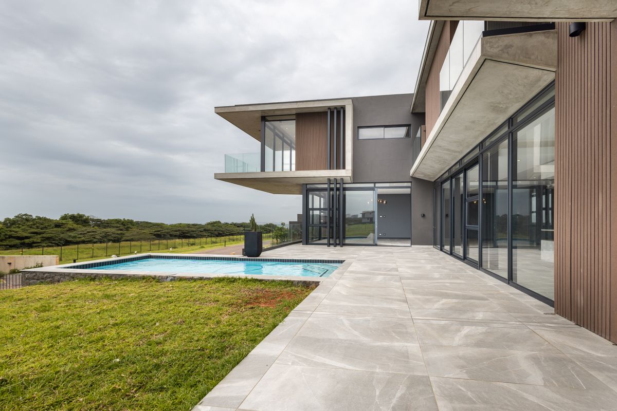 Modern rear elevation featuring a tiled patio, swimming pool, and expansive glass sliding doors opening to a contemporary architectural design.