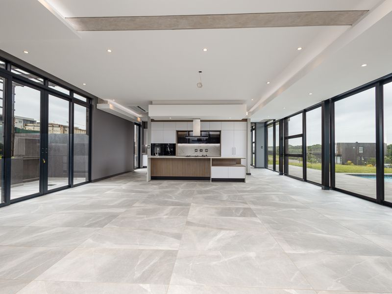 Spacious open-plan living and kitchen area featuring large format floor tiles, modern cabinetry, and expansive glass sliding doors leading to the outdoor pool area.