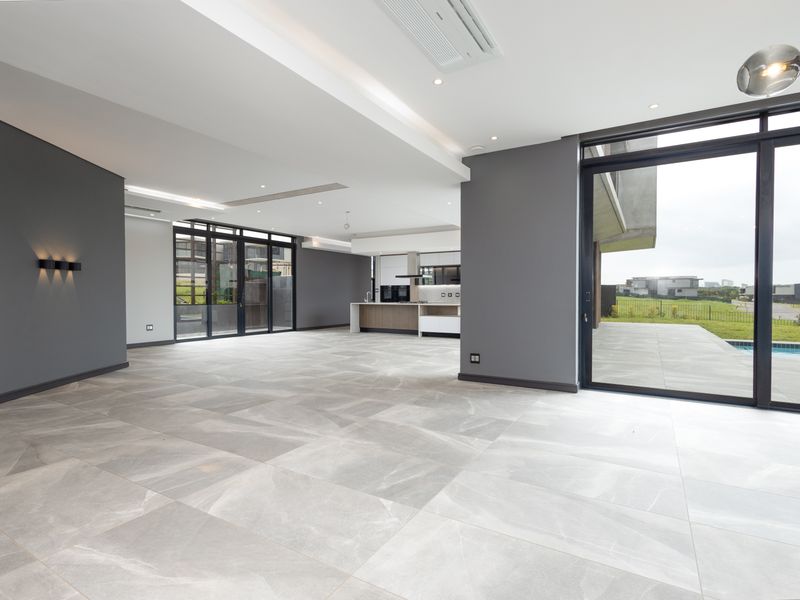 Spacious open-plan living and kitchen area featuring large-format porcelain tiles, modern recessed lighting, ducted air conditioning, and seamless access to the outdoor patio.