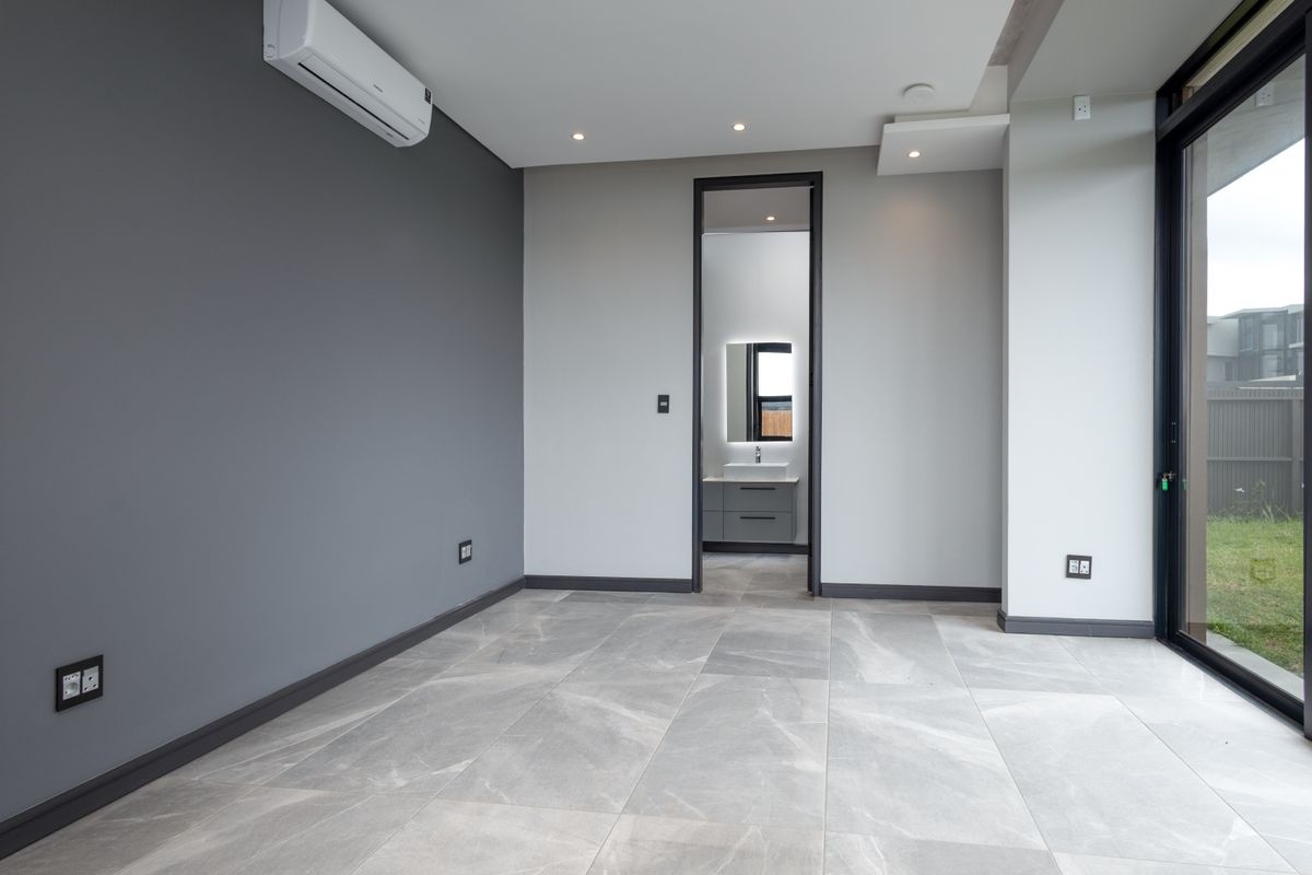 A modern, empty bedroom featuring large format floor tiles, recessed lighting, a split-system air conditioner, and direct access to the garden through a sliding door.