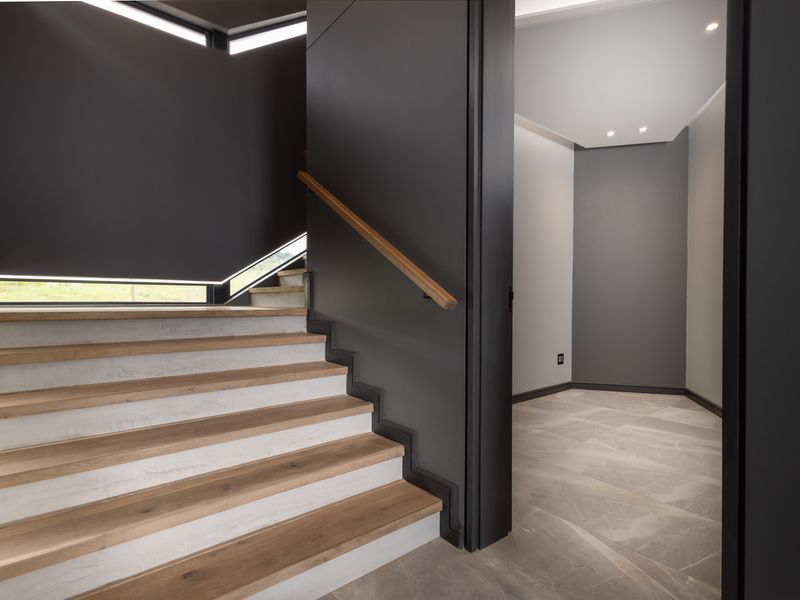 Modern hallway featuring a timber staircase with integrated lighting, sleek dark wall finishes, and neutral tiled flooring.