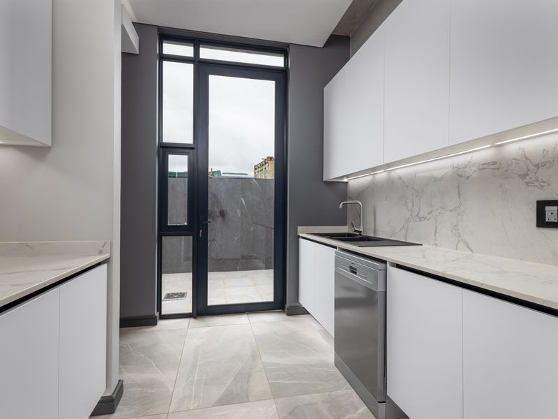 Modern scullery featuring sleek white cabinetry, marble-look stone countertops, integrated dishwasher, and direct access to an outdoor area.