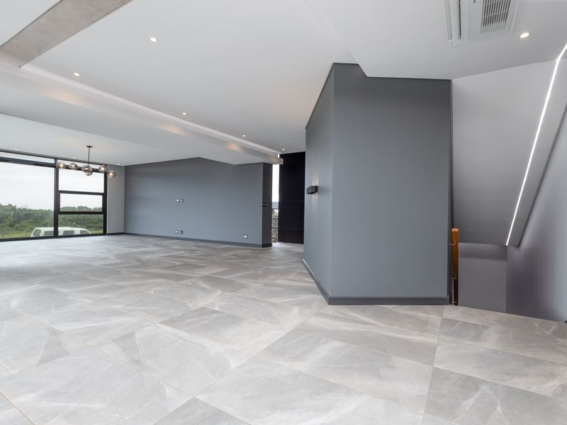 Spacious, modern open-plan living area featuring large format porcelain tiles, recessed lighting, and a sleek staircase with integrated LED accents.