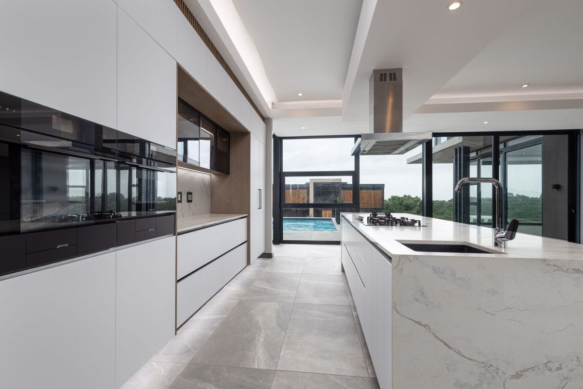 Modern luxury kitchen featuring a large stone-topped island, integrated appliances, sleek cabinetry, and floor-to-ceiling windows overlooking the pool area.