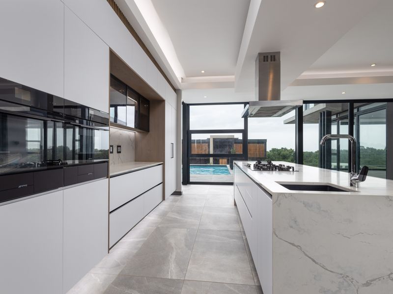 Modern luxury kitchen featuring a large stone-topped island, integrated appliances, sleek cabinetry, and floor-to-ceiling windows overlooking the pool area.
