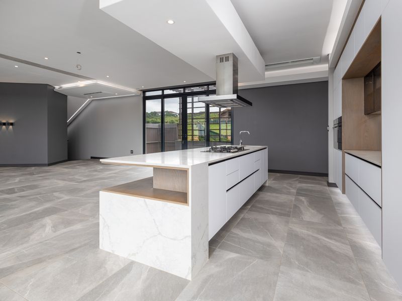 Modern open-plan kitchen featuring a large stone-topped island, integrated appliances, sleek cabinetry, and large format floor tiles leading to outdoor access.