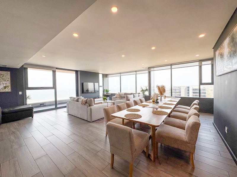 Spacious open-plan living and dining area featuring modern wood-look tile flooring, recessed lighting, and expansive floor-to-ceiling windows with abundant natural light.