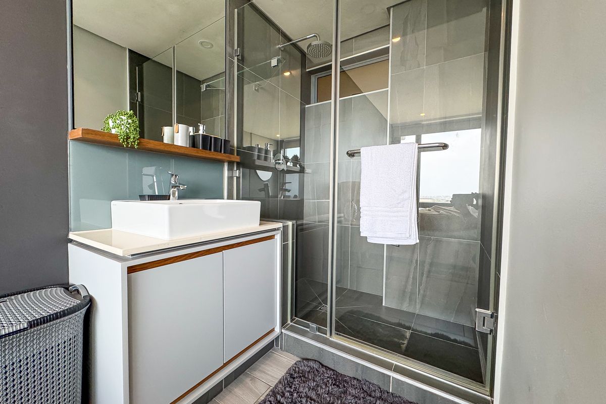 Modern bathroom featuring a vessel sink vanity, a glass-enclosed shower with a rain shower head, and contemporary grey tiling.