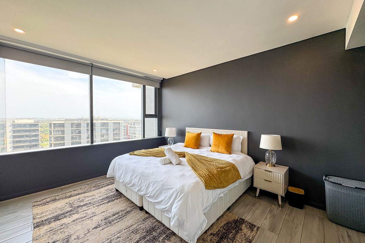 A modern bedroom featuring large floor-to-ceiling windows with expansive city views, recessed lighting, and neutral wood-look tile flooring.