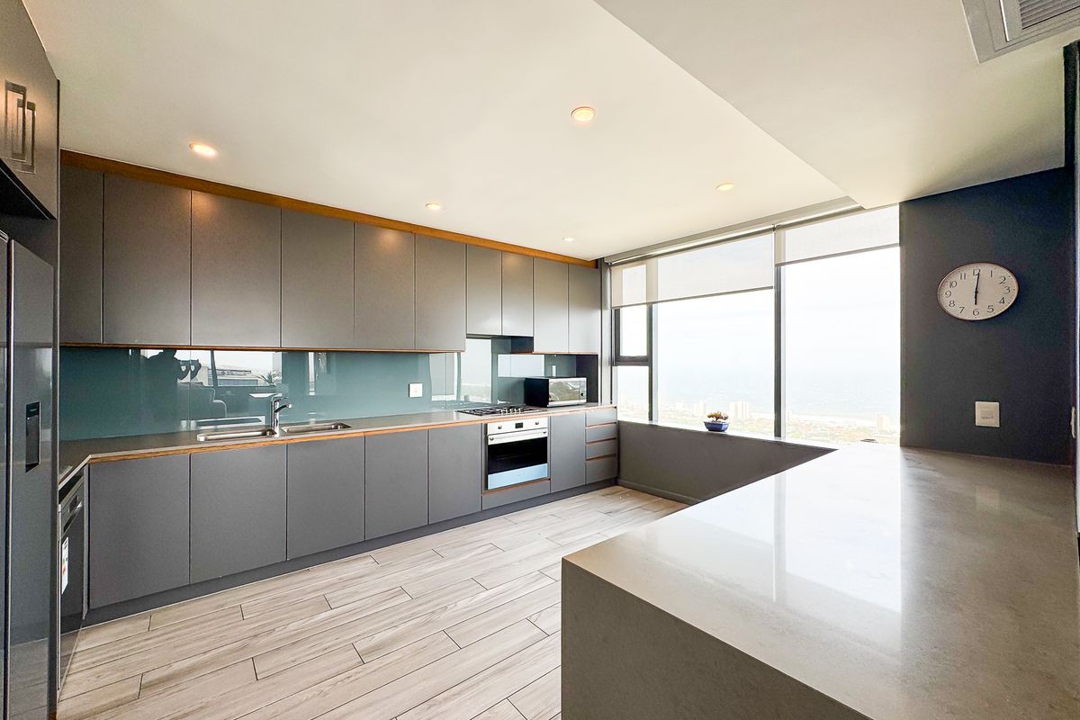 Modern kitchen featuring sleek grey cabinetry, stone countertops, integrated appliances, and large windows offering expansive coastal views.