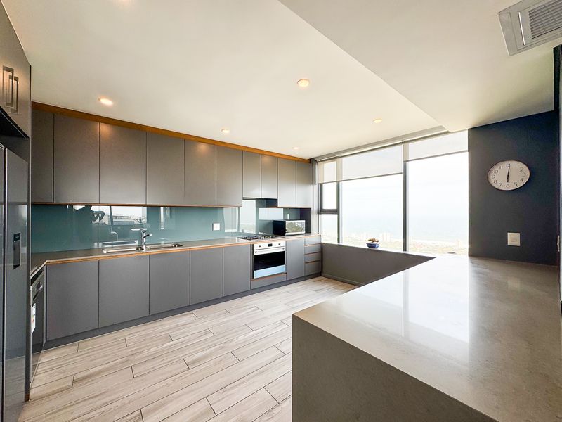 Modern kitchen featuring sleek grey cabinetry, stone countertops, integrated appliances, and large windows offering expansive coastal views.