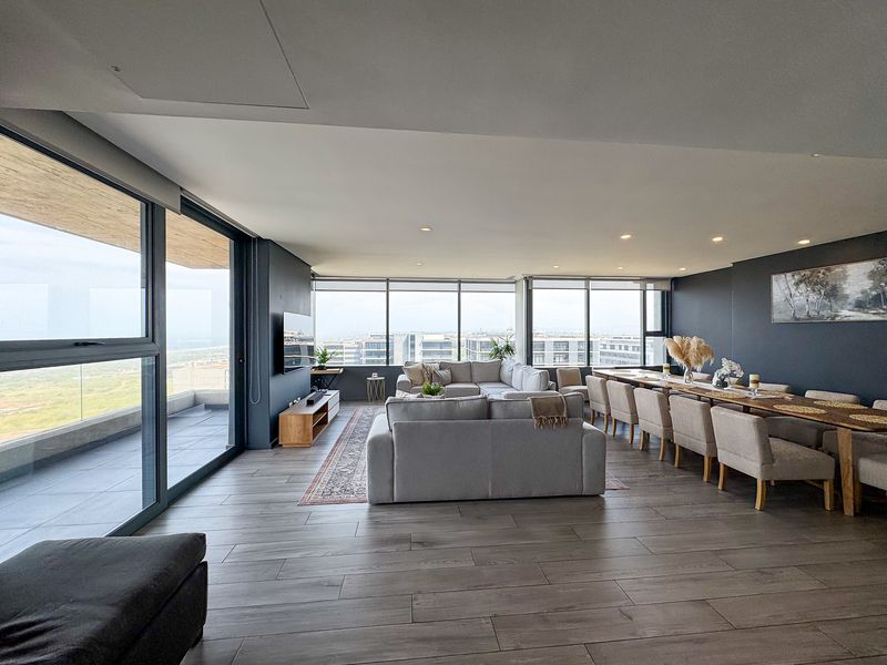 Spacious open-plan living and dining area featuring large-format floor tiles, expansive floor-to-ceiling windows, and seamless access to a private balcony with panoramic views.