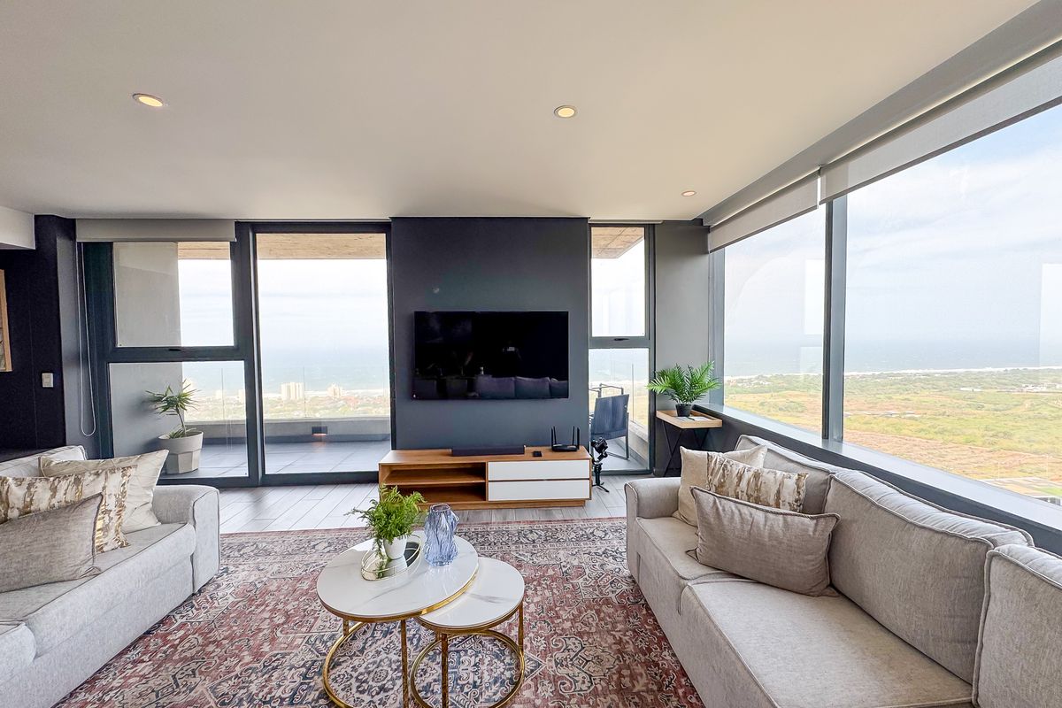 Modern living room featuring expansive floor-to-ceiling windows with panoramic coastal views, sleek tiled flooring, and recessed lighting in a contemporary apartment setting.
