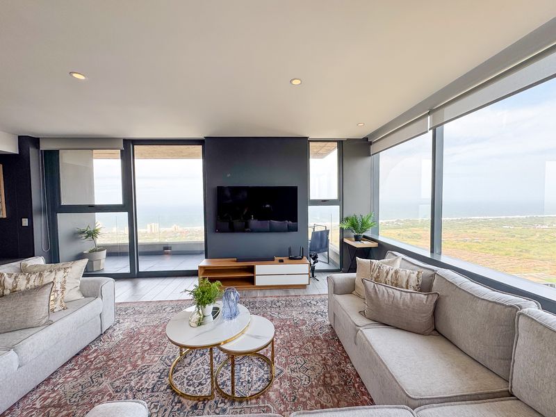 Modern living room featuring expansive floor-to-ceiling windows with panoramic coastal views, sleek tiled flooring, and recessed lighting in a contemporary apartment setting.
