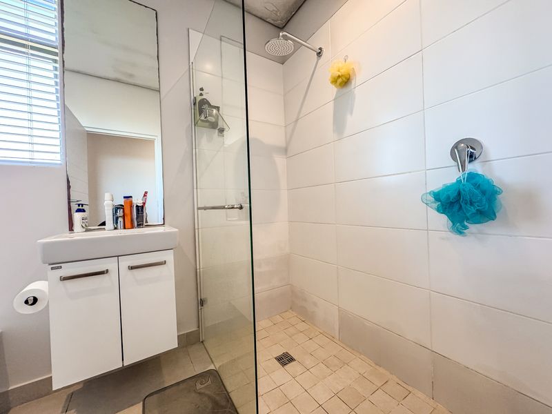A functional bathroom featuring a glass-enclosed shower, wall-mounted vanity, and large mirror, with some visible wear on the ceiling and tiling.