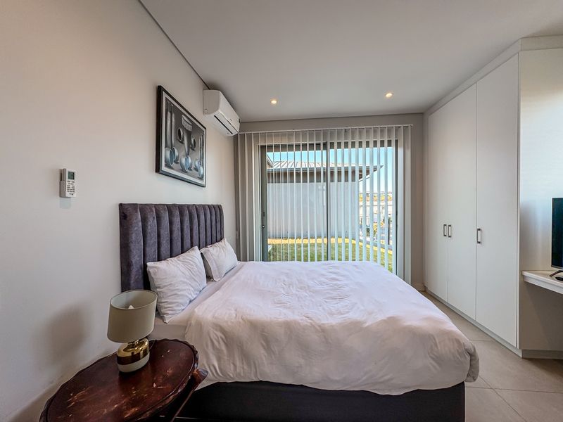 Modern bedroom featuring built-in cupboards, tiled flooring, split-system air conditioning, and a sliding glass door providing access to the exterior.