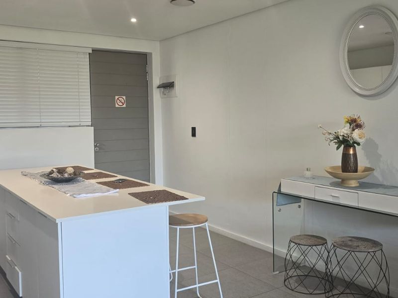 An open-plan living area featuring a central kitchen island, tiled flooring, recessed lighting, and neutral finishes, providing a versatile space for dining or food preparation.