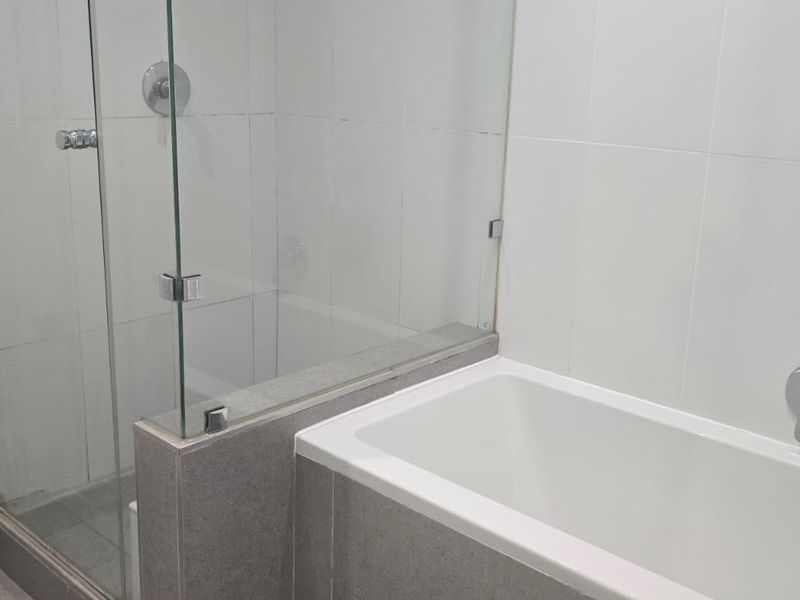 A clean bathroom featuring a glass-enclosed shower and a separate built-in bathtub with modern chrome fixtures and neutral wall tiling.