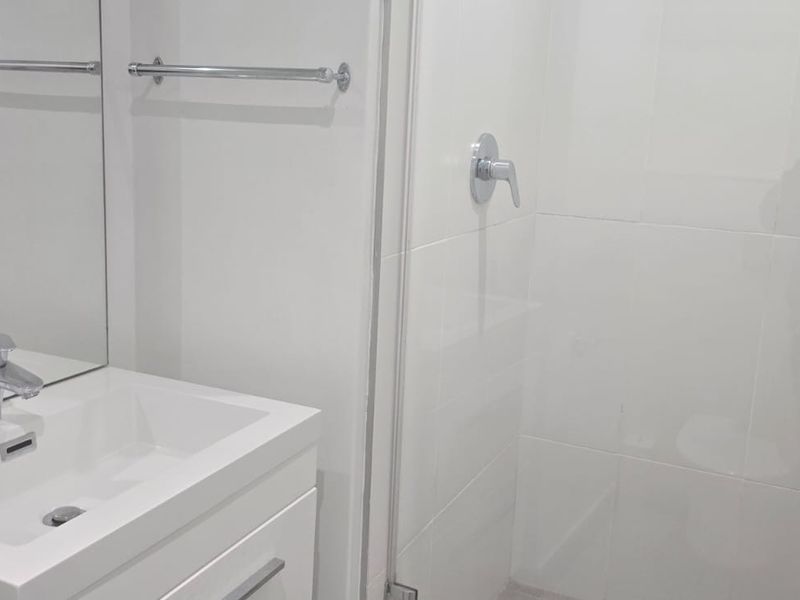 A clean, modern bathroom featuring a white vanity with basin, chrome mixer tap, towel rail, and a glass-enclosed shower with white wall tiles.