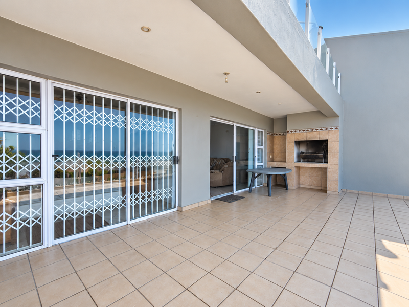 Spacious covered balcony featuring tiled flooring, a built-in braai, and sliding glass doors with security gates, offering an ideal space for outdoor entertaining.