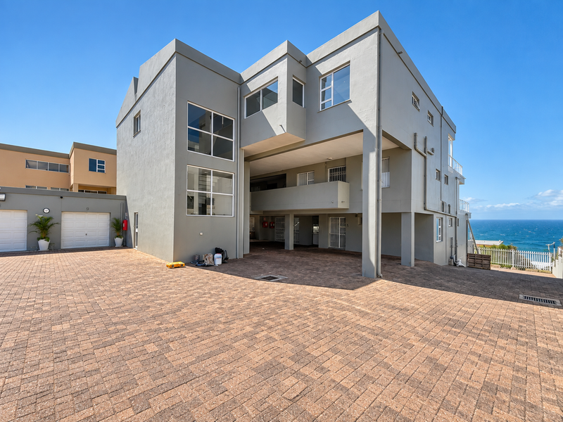 Modern multi-story apartment building exterior featuring a paved driveway, integrated garage access, and balconies with ocean views.