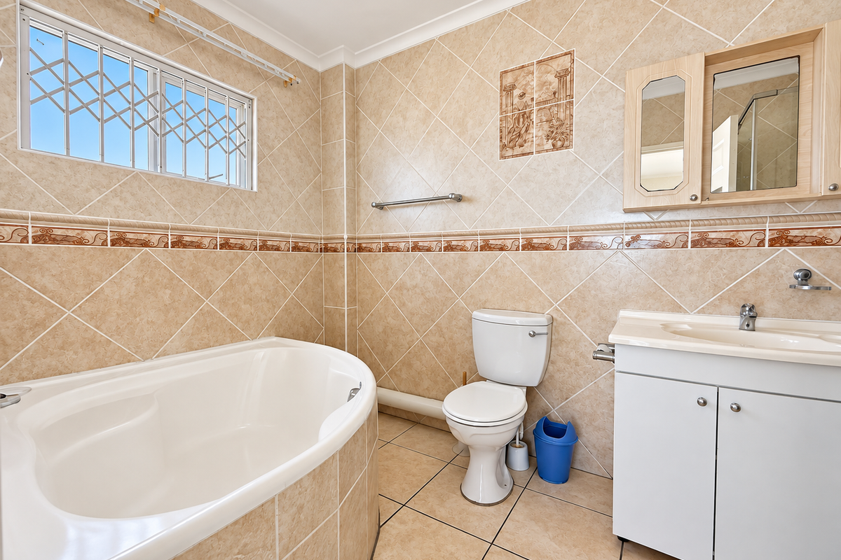 A functional bathroom featuring a built-in bathtub, vanity cabinet with washbasin, toilet, and neutral tiled finishes throughout.