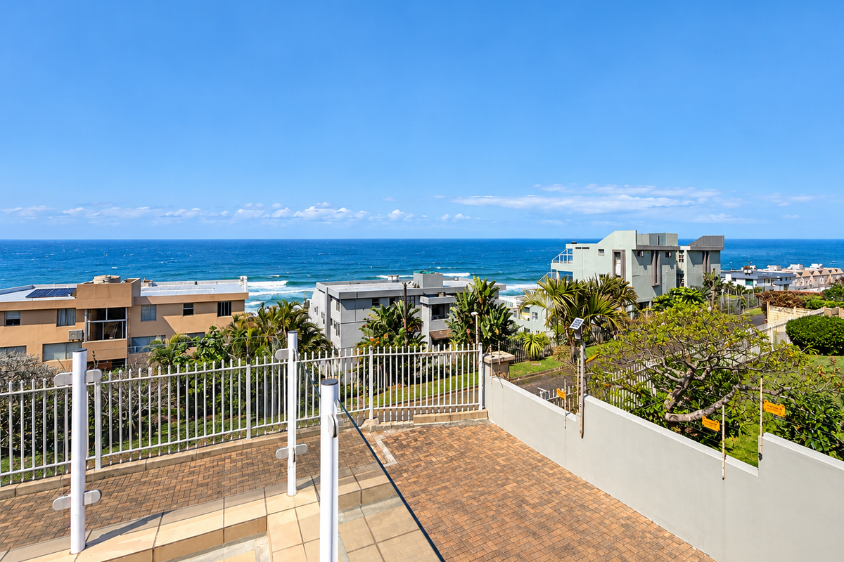 Elevated outdoor terrace featuring paved flooring and metal security fencing, offering expansive, unobstructed views of the ocean and surrounding coastal neighborhood.