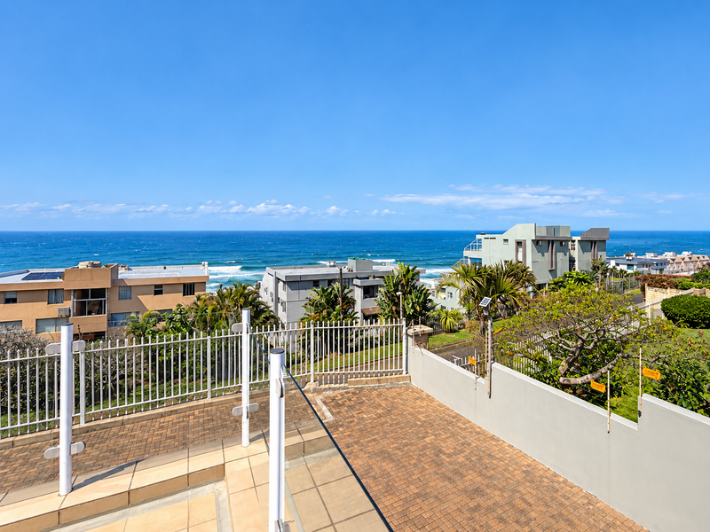 Elevated outdoor terrace featuring paved flooring and metal security fencing, offering expansive, unobstructed views of the ocean and surrounding coastal neighborhood.