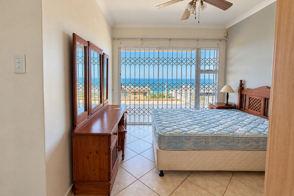A bedroom featuring tiled flooring, a ceiling fan, and a sliding door with a security gate, offering a view of the ocean.