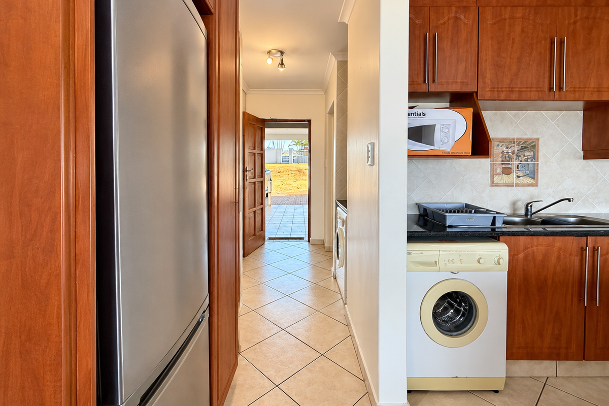 A functional kitchen area featuring wood-finish cabinetry, tiled backsplash, and integrated laundry plumbing, leading through to an exterior entrance.
