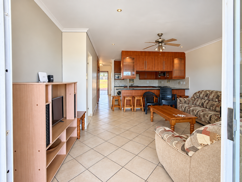 Open-plan living and kitchen area featuring tiled flooring, a breakfast bar, and wooden cabinetry, offering a functional layout with direct access to the exterior.